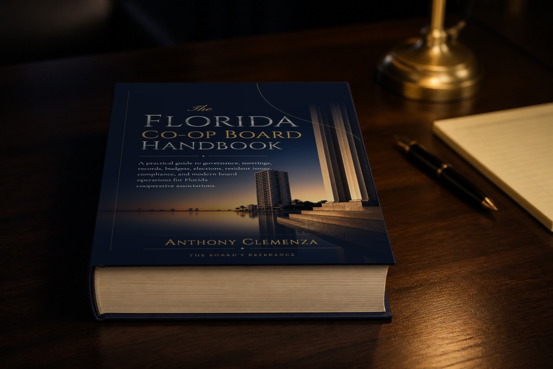 The casewrap hardcover closed on a walnut boardroom table beside a brass lamp, a fountain pen, and a legal pad at dusk